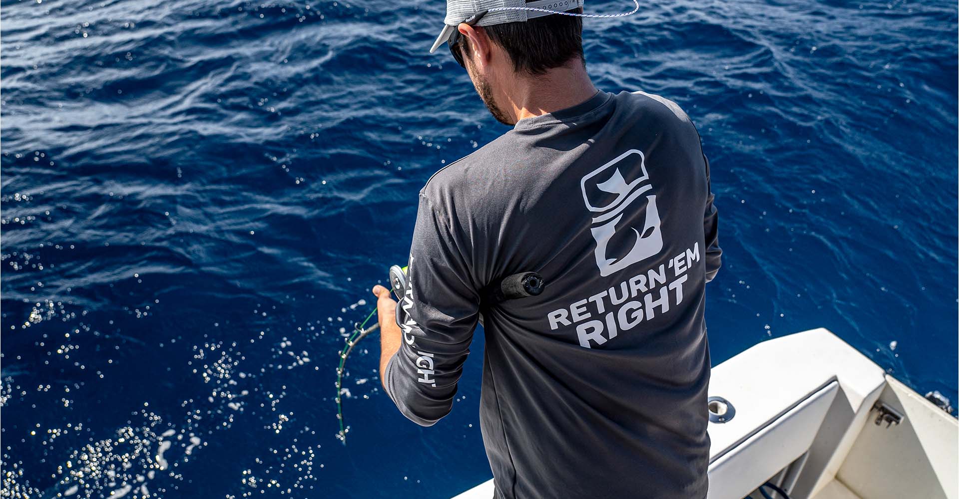Man on a boat holding a fishing pole with a shirt that says Return 'Em Right