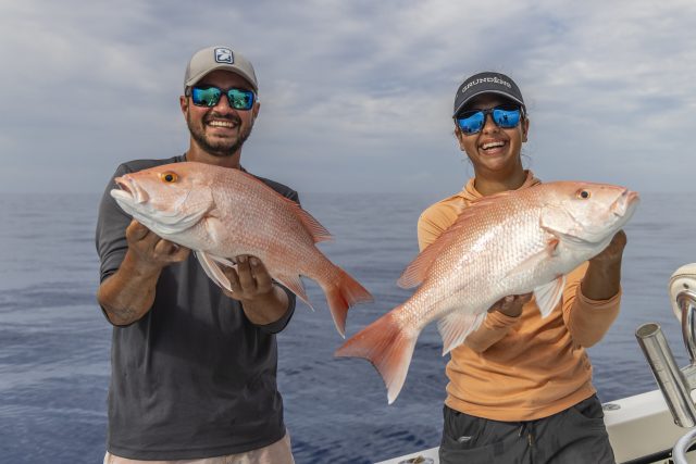Two anglers holding the red snappers that they caught.