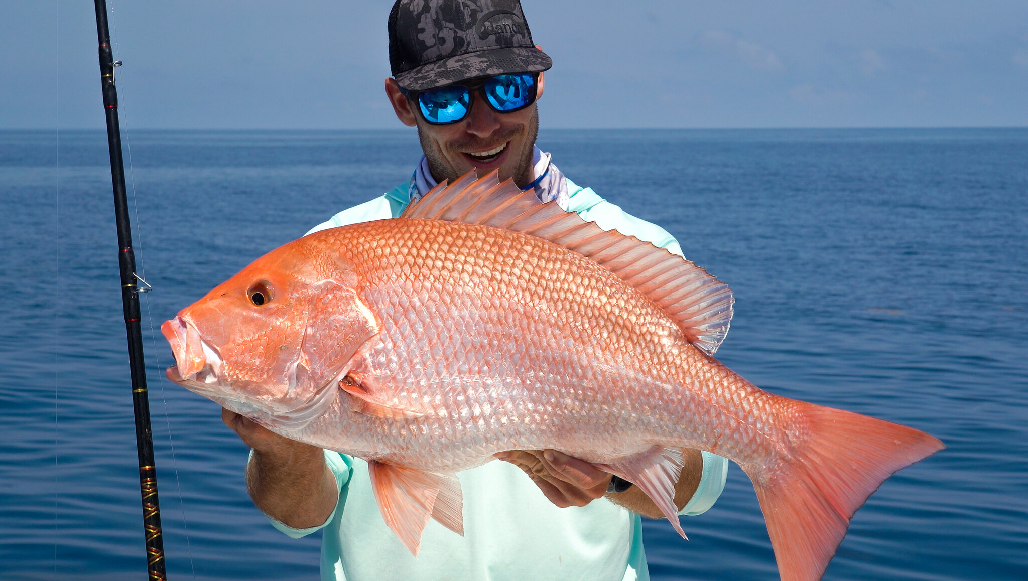 Ryan Morie standing on a boat, holding a Red snapper he caught.