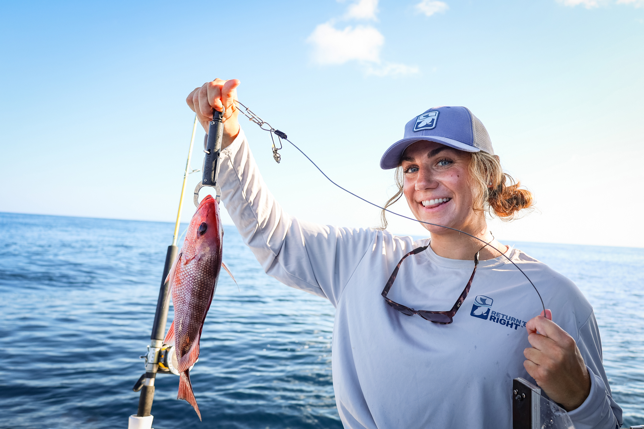An angler on a boat, holding a Red snapper that is attached to a descending device.