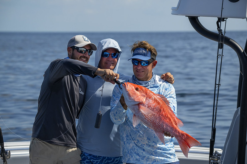 Anglers stand on a boat holding a Red snapper attached to a descending device.